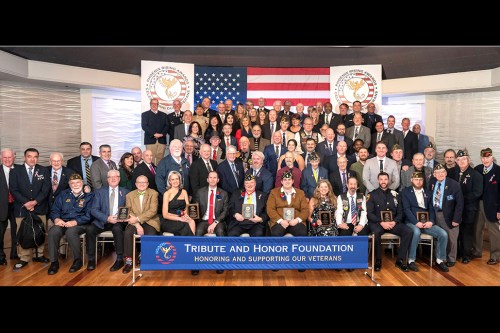 GC_tributeandhonor Honorees are seated, left to right, Howard Stillwagon (accepting on behalf of Dave Christie), Honor Flight Long Island represented by Roger Kilfoil and Bill Jones, Jenny and Sefan Hespeler, Anthony Anzalone, Luke Whitting, Lisa and Wayne Cohen, Derek Valance, and Chad Ryals. Standing immediately behind the honorees are veterans in attendance and on the risers are members of the Glen Cove Police and Fire Departments, Board and Liaison Members of the Tribute and Honor Foundation, and Mayor Pam Panzenbeck and other elected officials. (Photos provided by Adrienne Daley Photography)