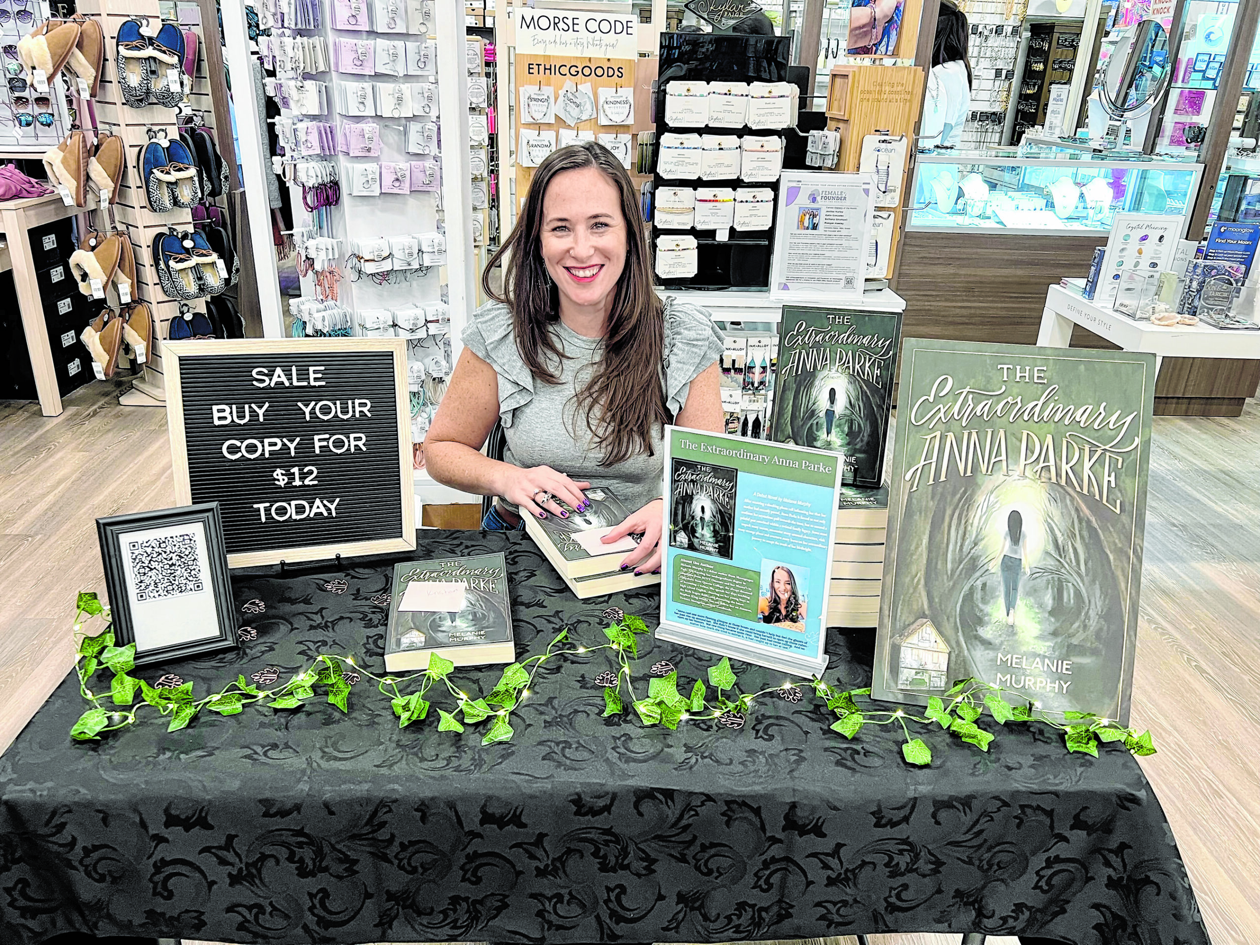 A female teacher sits at a table covered in her new book.