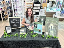 A female teacher sits at a table covered in her new book.