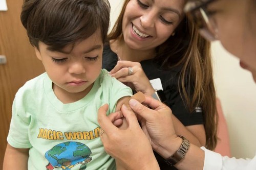 A young child sits on his mom’s lap while being vaccinated against childhood illnesses.
(Public domain via rawpixel)
