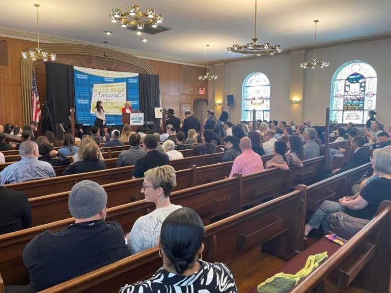 GoodDeeds_Cover Audience members watch Nassau County Comptroller Elaine Phillip present Roslyn High School student Emma Cohen with her award. (Photo courtesy Senator Steve Rhoads’ account on Facebook)
