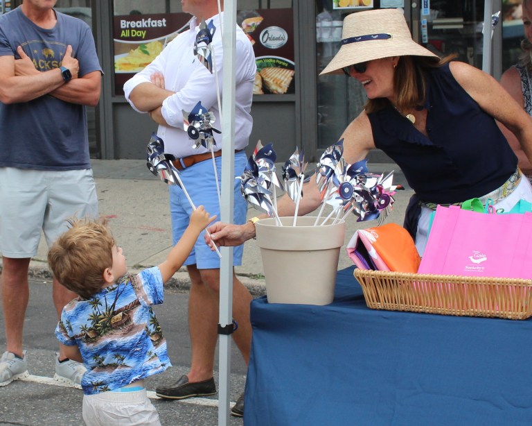 A woman at the Daniel Gale Sotheby's International Real Estate booth hands a pinwheel to a boy.